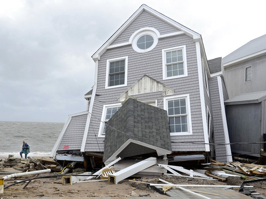 A woman walks past a house that collapsed during Superstorm Sandy in East Haven, Conn.