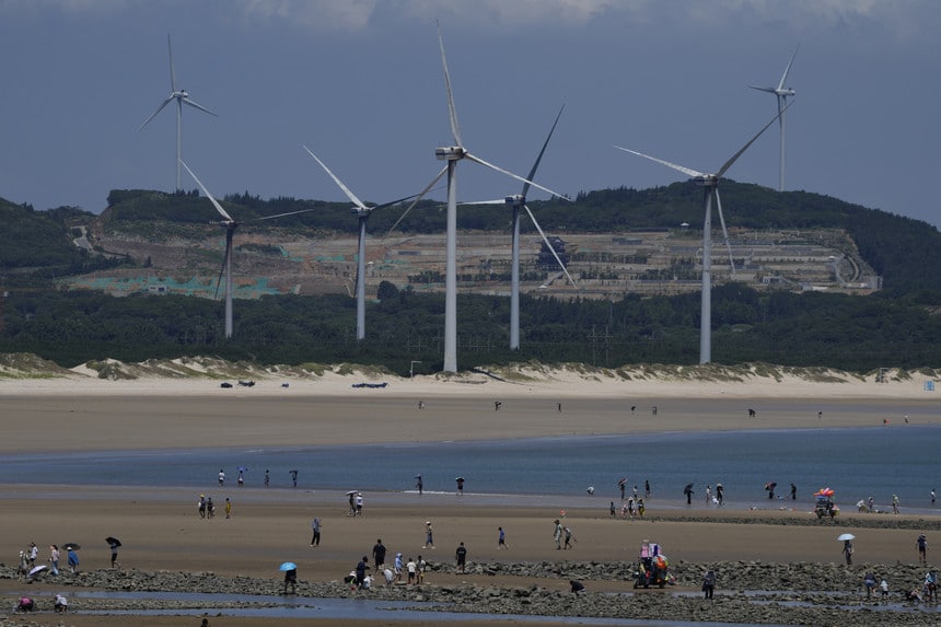 Beachgoers walk near wind turbines along the coast of Pingtan in Southern China's Fujian province.